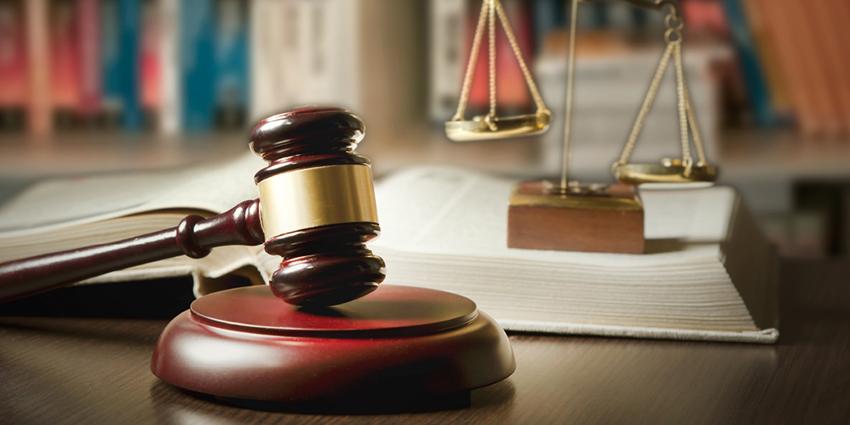 The image shows a judge's gavel and scales of justice on a desk with an open law book in the background, symbolizing the legislative and judicial framework.