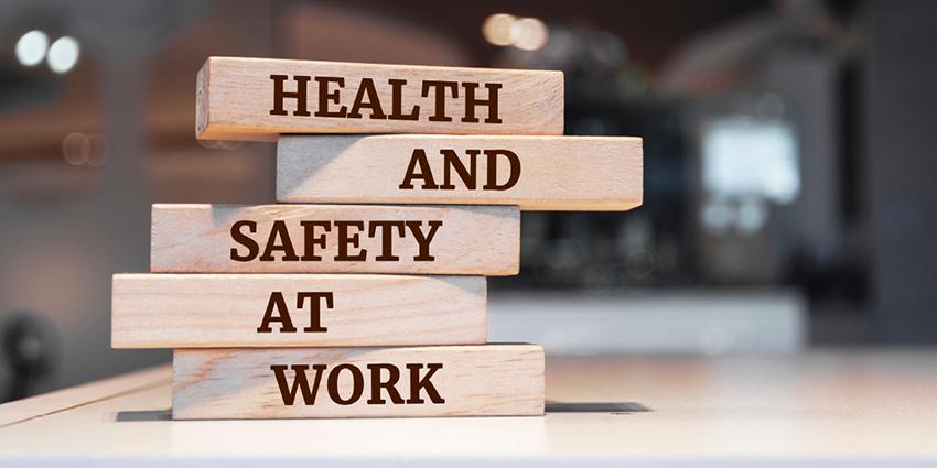 The image shows wooden blocks stacked on top of each other, with the words "HEALTH AND SAFETY AT WORK" printed in bold text across the blocks.